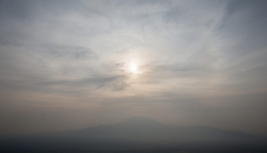 Hazy sky near sunset suggesting atmospheric aerosols over a distant mountain horizon